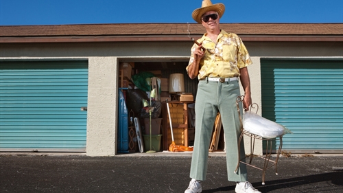 A man in a yellow shirt and white hat holding a chair in front of a storage unit. A man in a yellow shirt and white hat holding a chair in front of a storage unit.