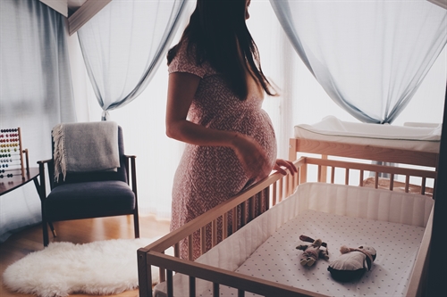 A pregnant woman waits near a cot in her babys nursery.