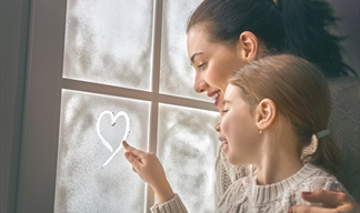 girl drawing a heart on frozen window with her mum in a warm December family scene.