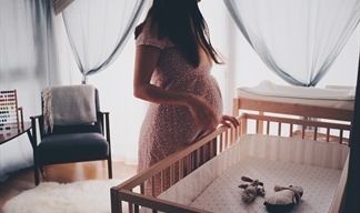 A pregnant woman waits near a cot in her babys nursery.